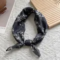 Detail of floral black chiffon neck scarf tied in a bow on a textured background - Black