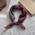 Close-up of vintage burgundy paisley silk scarf with artistic floral prints on a textured surface - Red