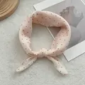 Close-up of a pink polka dot silk scarf tied in an elegant knot on a rustic background - Pink