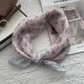 Détail d'un foulard floral en mousseline noué sur tissu blanc avec accessoires - Motif floral