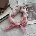 Detail of pink silk scarf with cat and cherry prints tied as a bow on a white knit blanket - Flower Cake