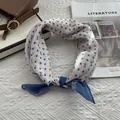 Close-up of a cream and blue polka dot silk scarf with bow patterns on a textured background - 58x58cm / Blue
