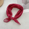 Detail view of red polka dot neck scarf with soft drape on a textured background - Red
