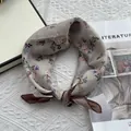 Detalle de un pañuelo de seda anudado con estampados florales vintage azul y naranja - Blanco Roto