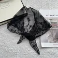 Detalle del delicado bordado floral negro en un pañuelo de encaje transparente - Negro