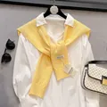 Detail of bright yellow knit shawl with hollow texture and handmade tag over white shirt - Yellow