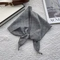 Detail of grey diamond-patterned cotton linen scarf tied on a white textured background - Gray