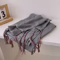 Detailed macro view of dark grey cotton linen scarf with red and white tassel accents - Gray