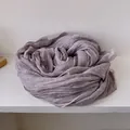 Dettaglio di una sciarpa di lino viola chiaro con bordi in pizzo su legno bianco - Viola
