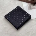 Close-up of a black and white polka dot cotton scarf folded on a soft white texture - Black