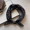Dettaglio di una sciarpa in chiffon nero con motivi floreali blu e viola su bianco - Nero