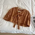 Detail of a brown cable knit short shawl with a decorative bow on a white background - Pumpkin Orange