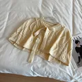Detail of cable knit beige short poncho with a decorative ribbon bow on a hanger - Off White