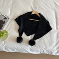 Detail of black knitted triangle scarf with soft pom-poms hanging on a wooden hanger - Black