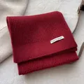 Close-up of deep red ribbed knit scarf with designer fabric label on wool texture - Ancorra Red