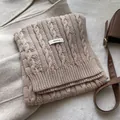 Close-up detail of beige cable knit wool scarf with 100% wool material label - Pink