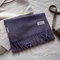 Nahaufnahme eines lila Wollschals mit Fransen, gewebtem Logo-Etikett und Anhänger - 180*30cm / Melange Lila