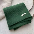 Detail eines dunkelgrünen Strickschals mit weißem Webetikett auf weichem Plüschgrund - Grün