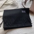 Detail of soft 100% pure wool black scarf featuring fringe edges and woven fabric label - 180*30cm / Black