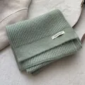 Detail eines hellgrünen Strickschals mit Waffelmuster und elegantem Markenetikett - Bohnengrün