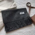 Detailansicht eines dunkelgrauen Wollschals mit Fransen und Textiletikett im Detail - 180*30cm / Melange Schwarz
