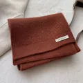 Detailstruktur des karamellfarbenen Waffelstrickschals aus Wolle mit weißem Aufnäher - Schokoladenbraun