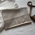 Detailaufnahme von beigem Wollschal mit Fransen und gewebtem Markenetikett - 180*30cm / Melange Milchtee