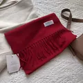 Nahaufnahme eines roten Schals aus reiner Wolle mit Fransen, Markenetiketten und Textur - 180*30cm / Melange Tomatenrot