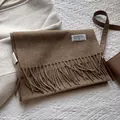 Detailaufnahme des braunen Wollschals mit Fransen und Markenlogo auf strukturierter Fläche - 180*30cm / Melange Bernstein