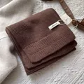 Detalle macro de bufanda de lana marrón oscuro que muestra el tejido y la etiqueta 100% - Café