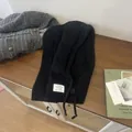 Detail of black wool balaclava scarf with buttons and label on a wooden cabinet - Black
