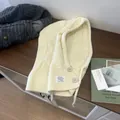 Detail der cremefarbenen Strick-Balaclava mit Knopfverschluss und dekorativem Etikett - Gebrochenes Weiß