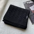 Detailed view of black cable-knit wool scarf with 100% wool label on textured fabric - Black