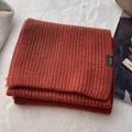 Detailed view of the 100% pure wool label on a rust red thick knit winter scarf - Orange