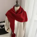 Close-up of bright red knitted scarf with soft fur pom-poms and winter coat texture - New Year Red