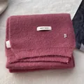 Detailed macro view of plum pink wool knit scarf with silver B pendant and fabric label - Rose Gold