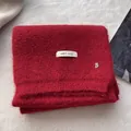 Detail of red wool knit scarf featuring a white woven label and silver metal B pendant - China Red