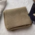 Detail eines kamelfarbenen Wollschals mit 100% Wolle-Etikett und Rippenstrick-Struktur - Tabak Kaffee