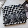 Detail of soft black and white houndstooth scarf texture with woven fringes and a fabric label - Navy Beige