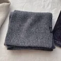 Detail eines Schals aus 100% Wolle mit grauer Rippenstruktur und Materialetikett - Grau