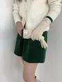 Nahaufnahme von Strickhandschuhen mit 'Bonjour'-Etikett und dunkelgrünen Strickbündchen - Gebrochenes Weiß