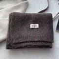 Detail of wool blend scarf with white woven label showing fine knit texture on plush background - Coffee