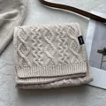 Close-up of cable knit texture on 100% merino wool scarf with premium woven brand label - Off White