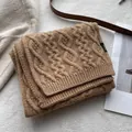 Detail of cable knit wool scarf in camel with a black label showing 100% wool material - Tobacco Coffee