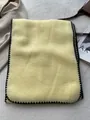 Detailed close-up of thick beige wool scarf with black whipstitch edge on textured carpet - 180*60cm / Milk Yellow