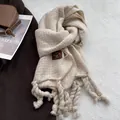 Primer plano de bufanda tejida beige con borlas y etiqueta de cuero marrón cosida - Crema