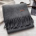 Close-up of dark grey wool scarf featuring long tassels and a brown leather patch - Dark Heather Gray