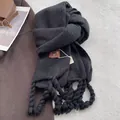 Close-up of thick tassels and branded leather tag on a heavy grey cashmere scarf - Black