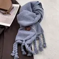 Detail of dusty blue knit scarf with chunky tassels and leather brand tag on coat - Azure Blue
