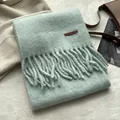 Détail d'une écharpe en maille vert clair avec de longues franges et étiquette en cuir - Vert frais